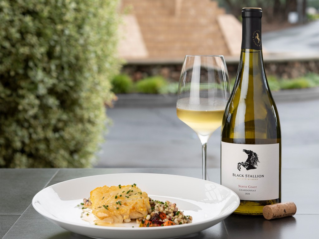 A bottle of Black Stallion Estate Winery North Coast Chardonnay next to a glass of wine and a plate of Pan Roasted Ling Cod with Citrus Beurre Blanc